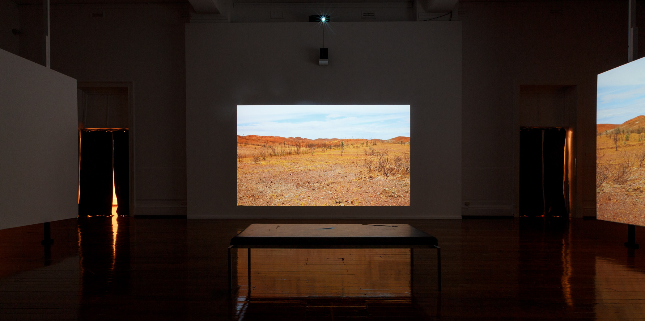 Melbourne-based artist Claire Robertson’s cinematic installation depicts an uninhabited temporary mining camp in the Pilbara, showing scenes of empty industrial villages set against the Australian outback. The installation is accompanied by a haunting original soundtrack by composer Tilman Robinson.