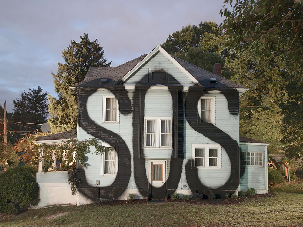 Ian Strange carried out a largescale intervention on this suburban American home, painting SOS in huge lettering on it side